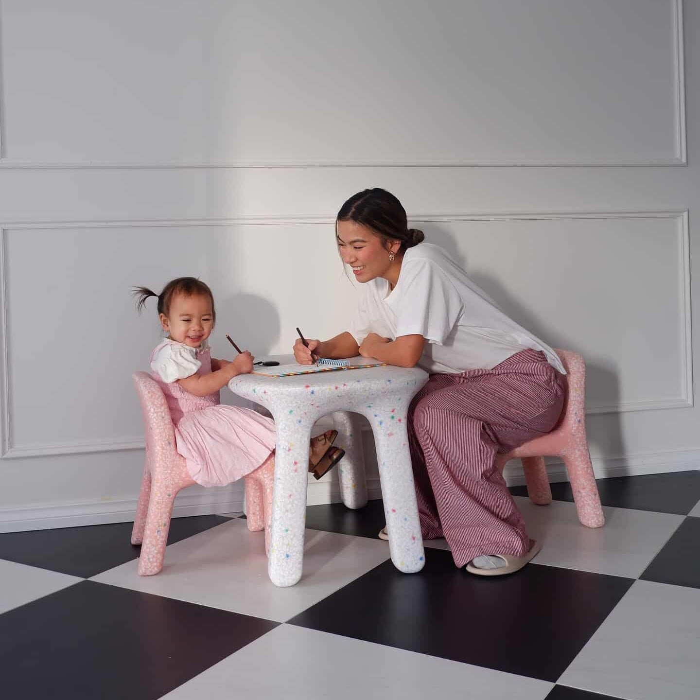 Woman and child sitting at a small table on a checkered floor with white walls.
