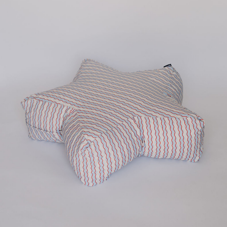 A star-shaped floor cushion with a white base and thin red and blue wavy stripes, photographed against a plain light gray background.
