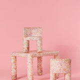 Floral-patterned chair and stool set against a pink background