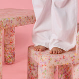 Children's legs on a colorful stool against a pink background