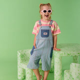 Child wearing sunglasses and a striped shirt with overalls standing on a green background