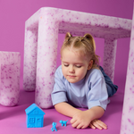 Child playing with toys on a pink floor with pink and white geometric structures in the background.