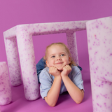 Child lying on a pink and white striped surface with a pink background