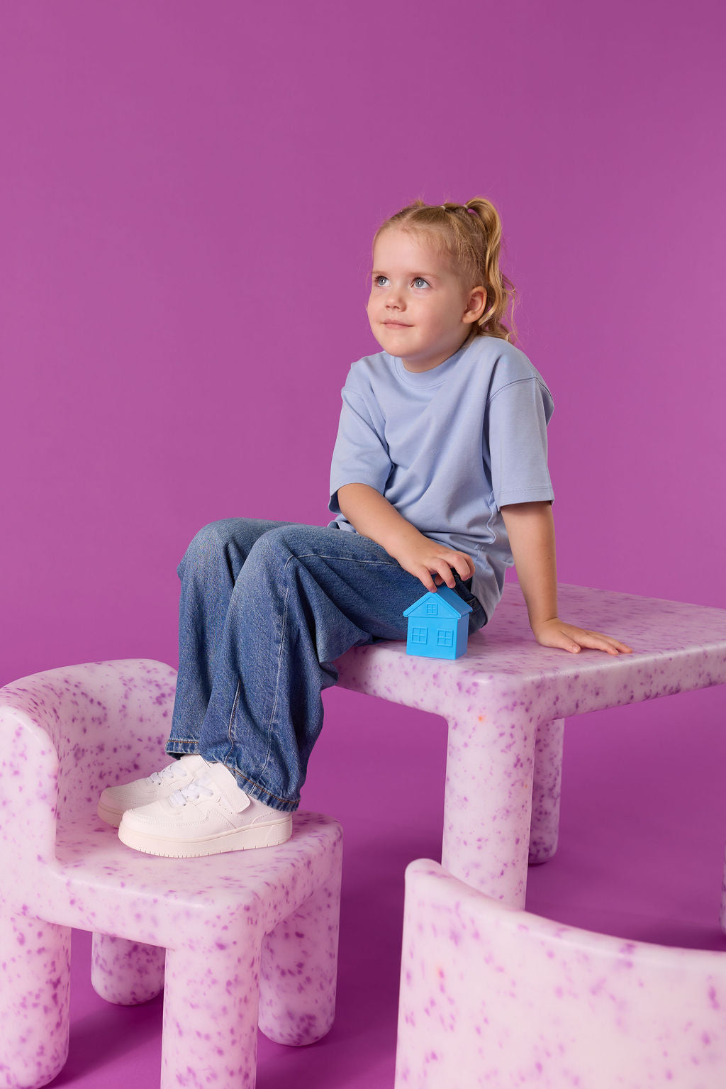 Child sitting on a pink chair with a purple background