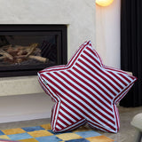 Red and blue striped star-shaped pillow on a checkered floor with a fireplace in the background.