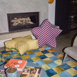 Living room with a colorful checkered rug, coffee table with magazines, and a striped pillow.