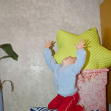 Child playing with colorful cushions on a striped ottoman against a textured wall.