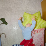 Child playing with colorful cushions on a striped ottoman against a textured wall.