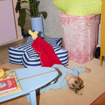 Child playing with a toy on the floor next to a striped chair and a plant.