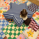 A young child sits on a large star-shaped floor cushion with navy and white stripes, placed on a colorful patchwork quilted play mat.