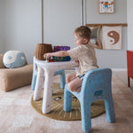 Child playing at a small table in a room with toys and colorful cushions.