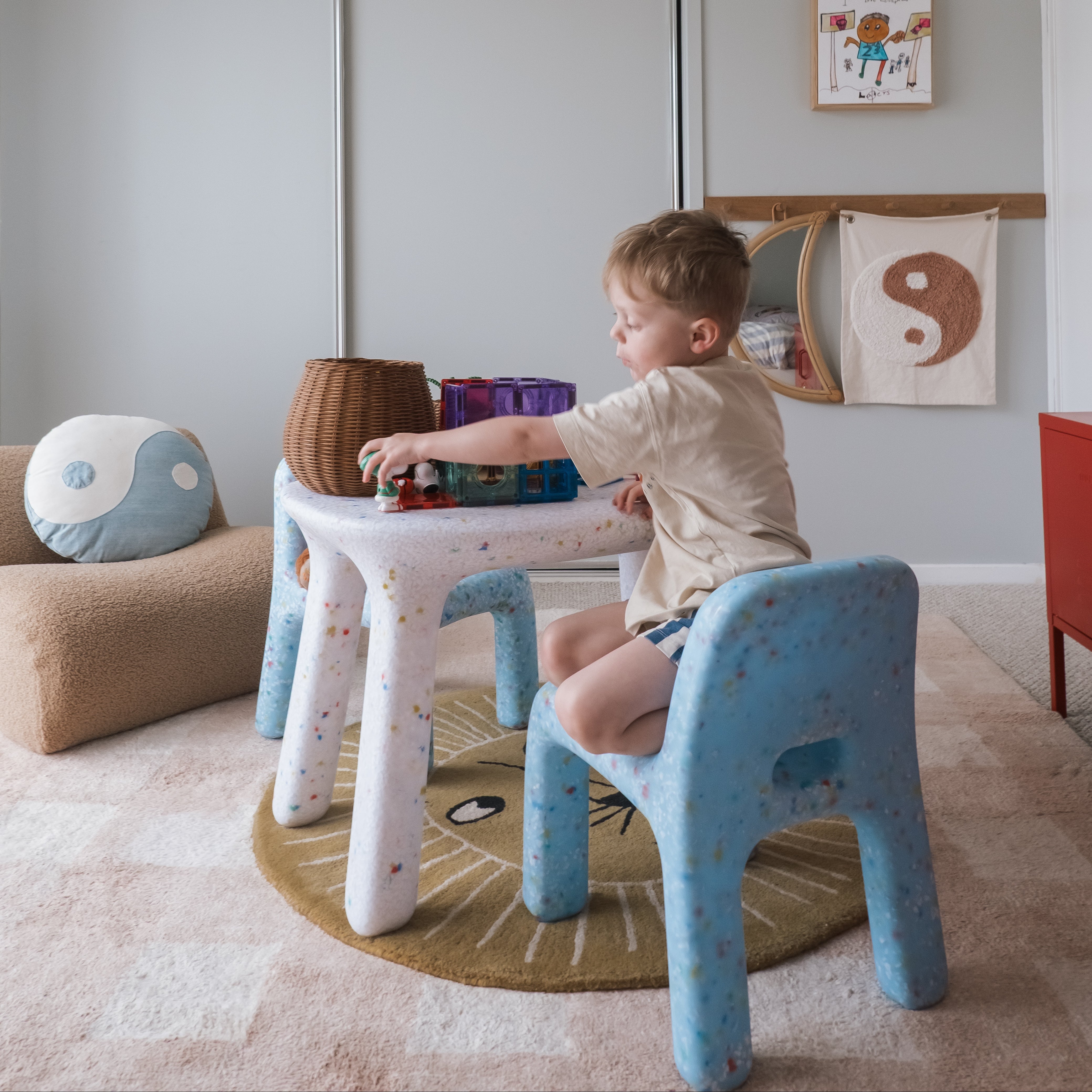Child playing at a small table in a room with toys and colorful cushions.