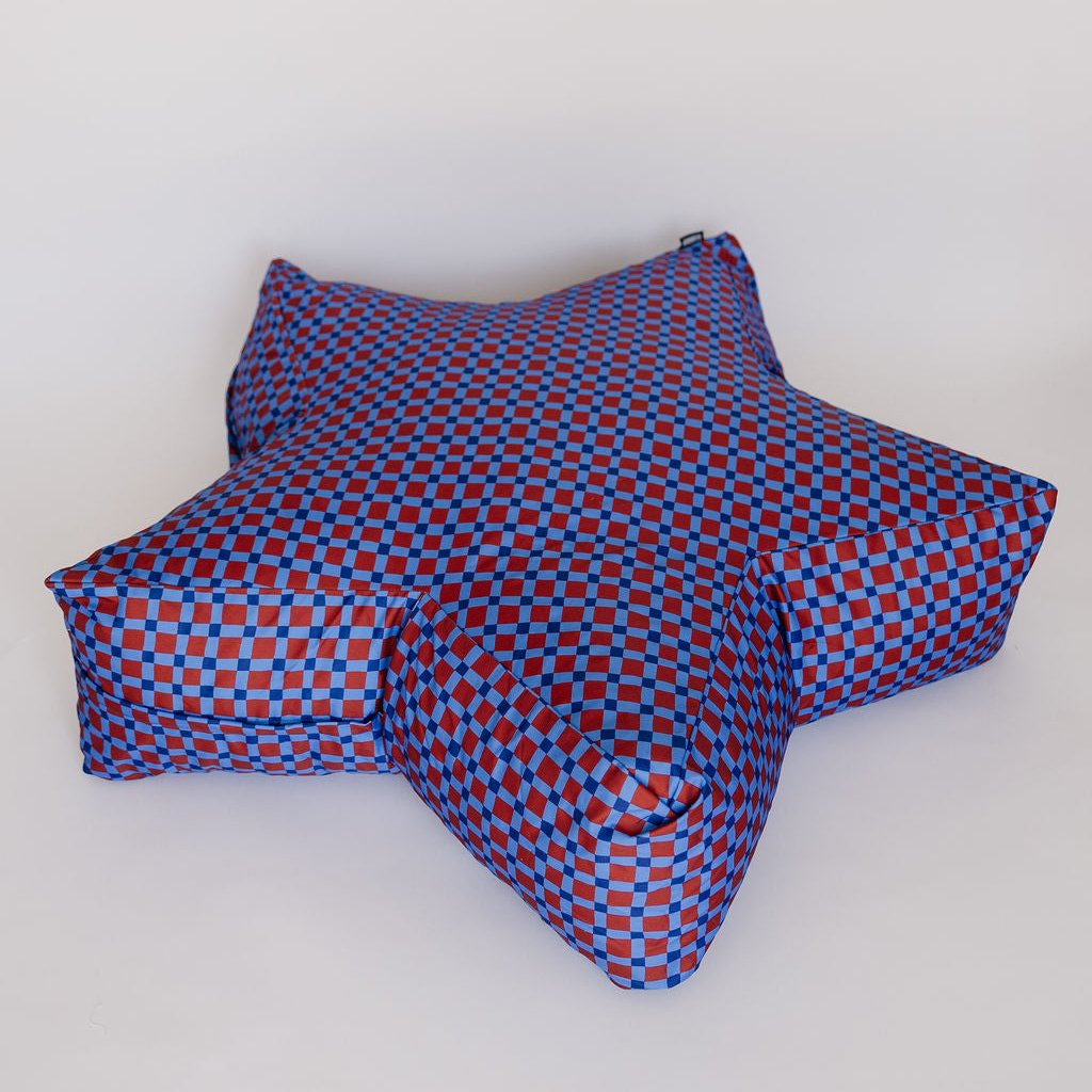 A star-shaped floor cushion with a blue and red checkerboard pattern, photographed on a plain light gray studio background.