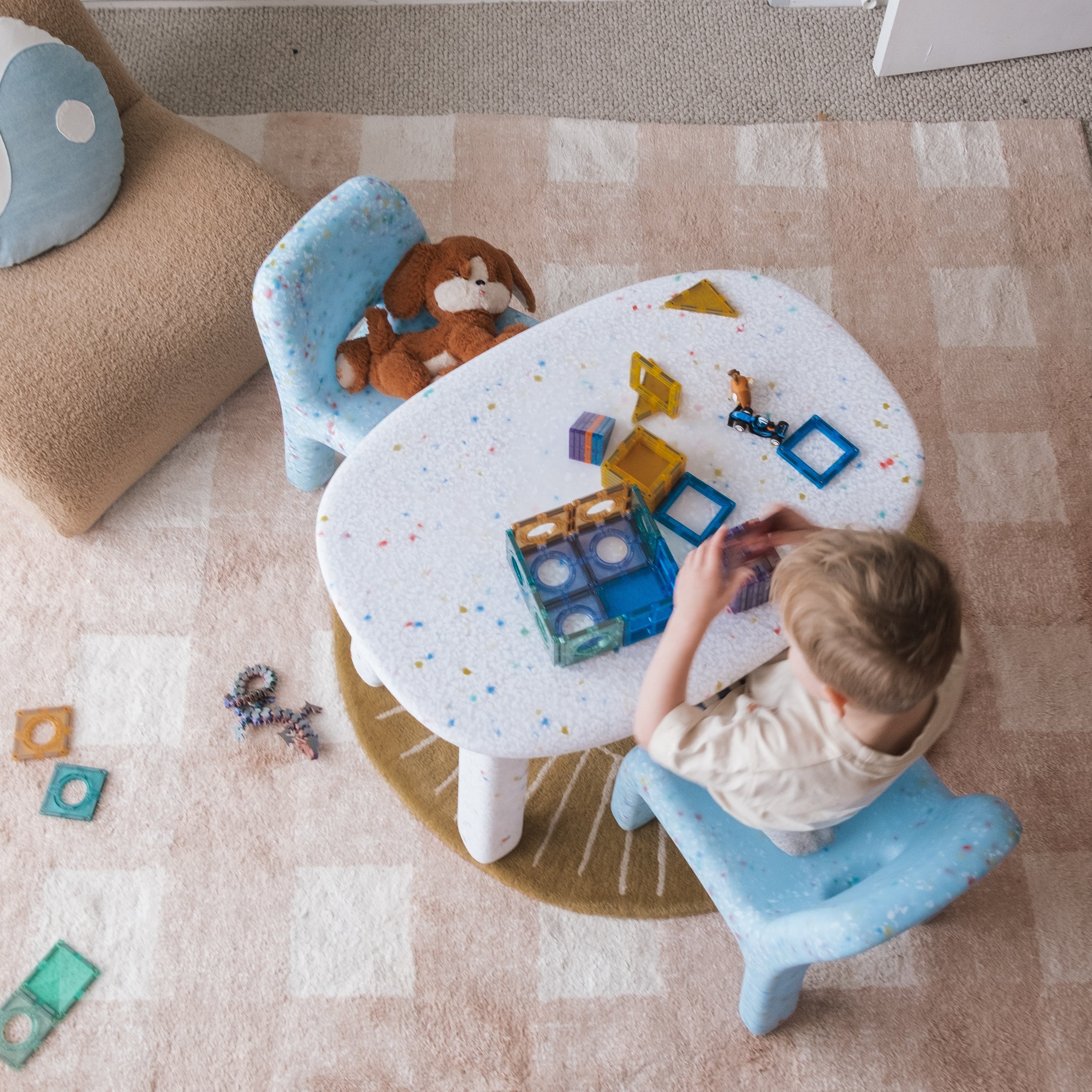 Child playing with toys on a small round table in a room with a carpeted floor.