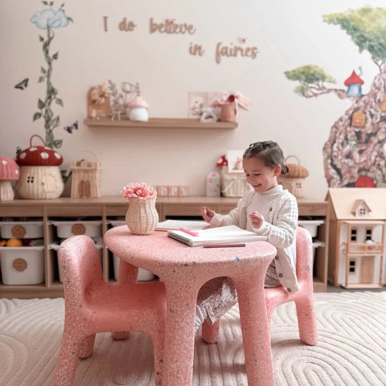 Child sitting at a pink table in a playroom with fairy-themed decor.
