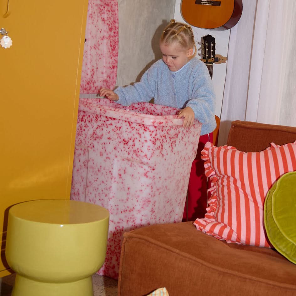 Child playing with a toy in a room with a guitar, colorful furniture, and a window.