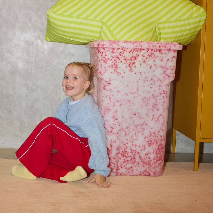 Child sitting on a star-shaped pillow with a pink base in a room.