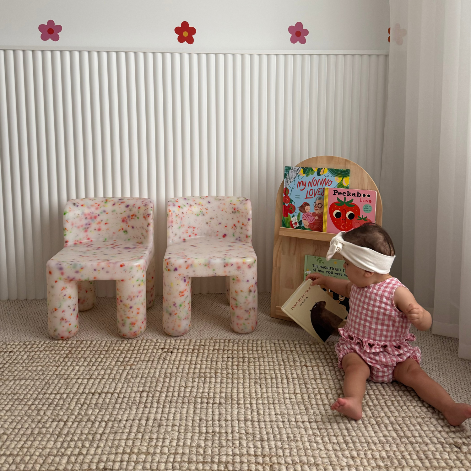 Child playing with books on a carpeted floor next to floral-patterned chairs.