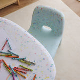 Colorful crayons on a polka dot table with a chair in the background