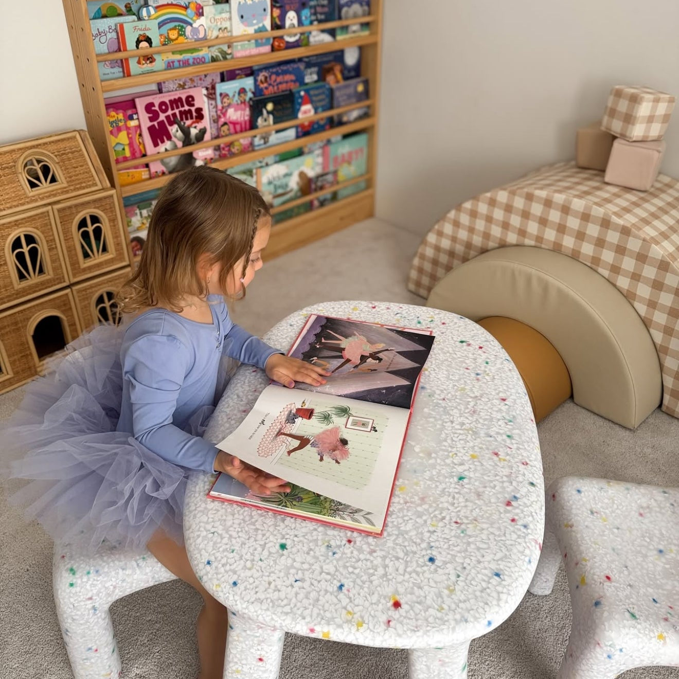 Child reading a book at a small table with a bookshelf filled with books in the background.