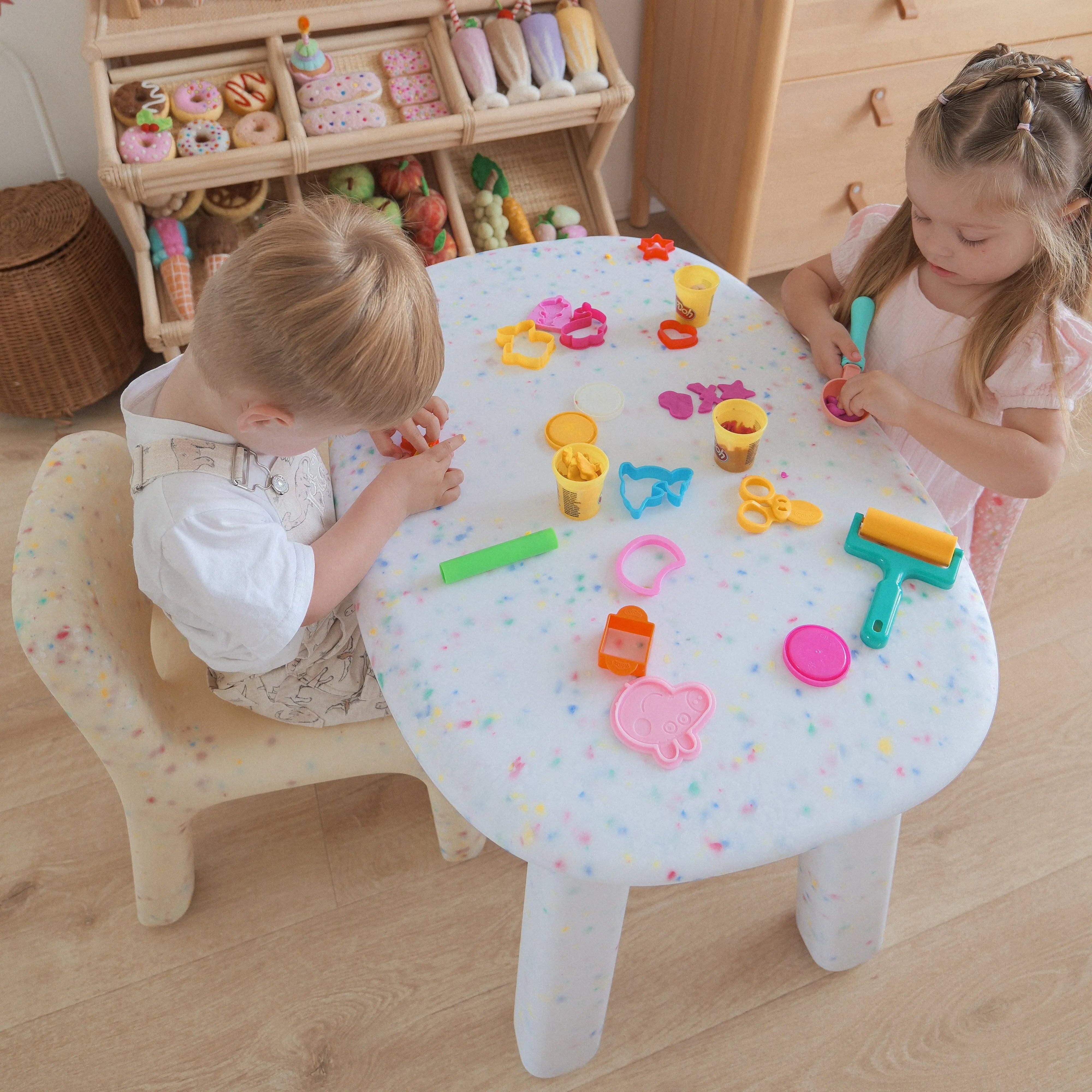 Two children playing with colorful toys on a small table in a room with wooden furniture.