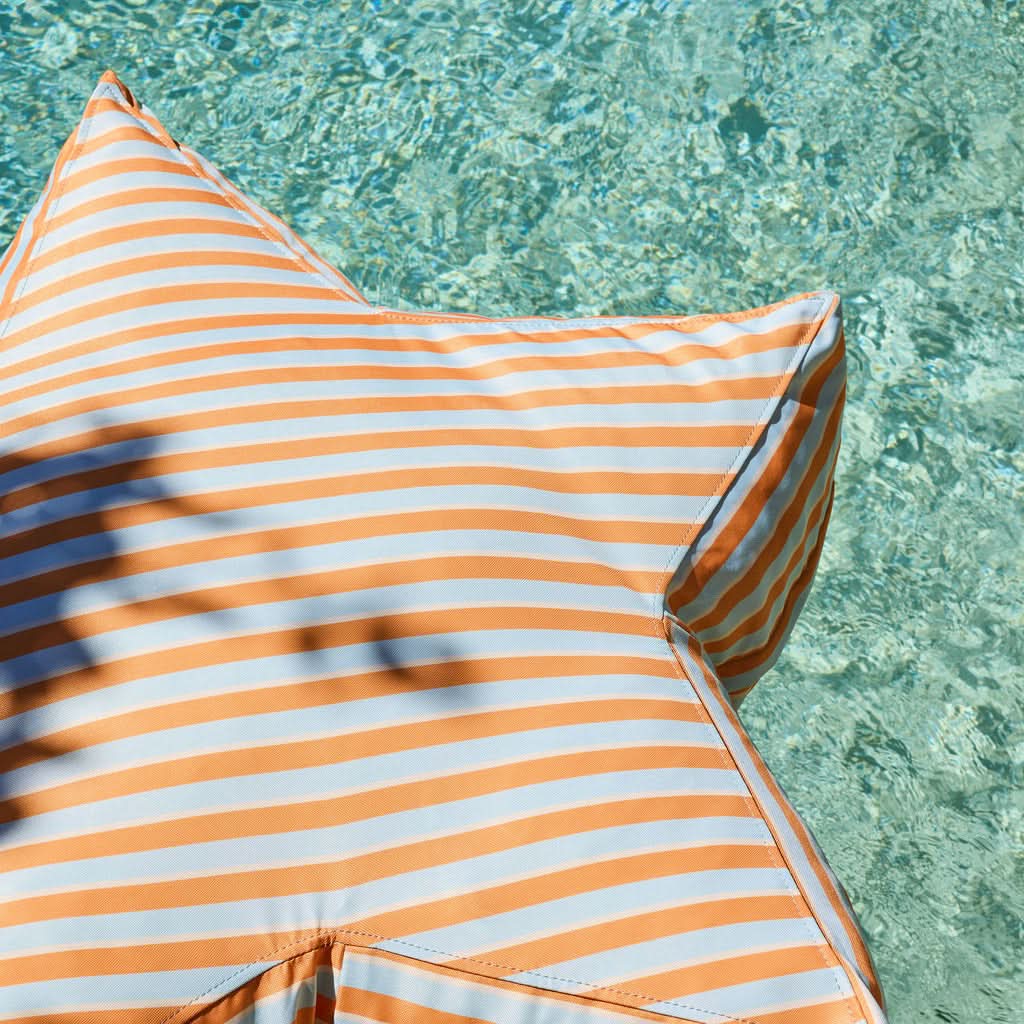 Orange and light blue + thin cream striped star pillow by a pool
