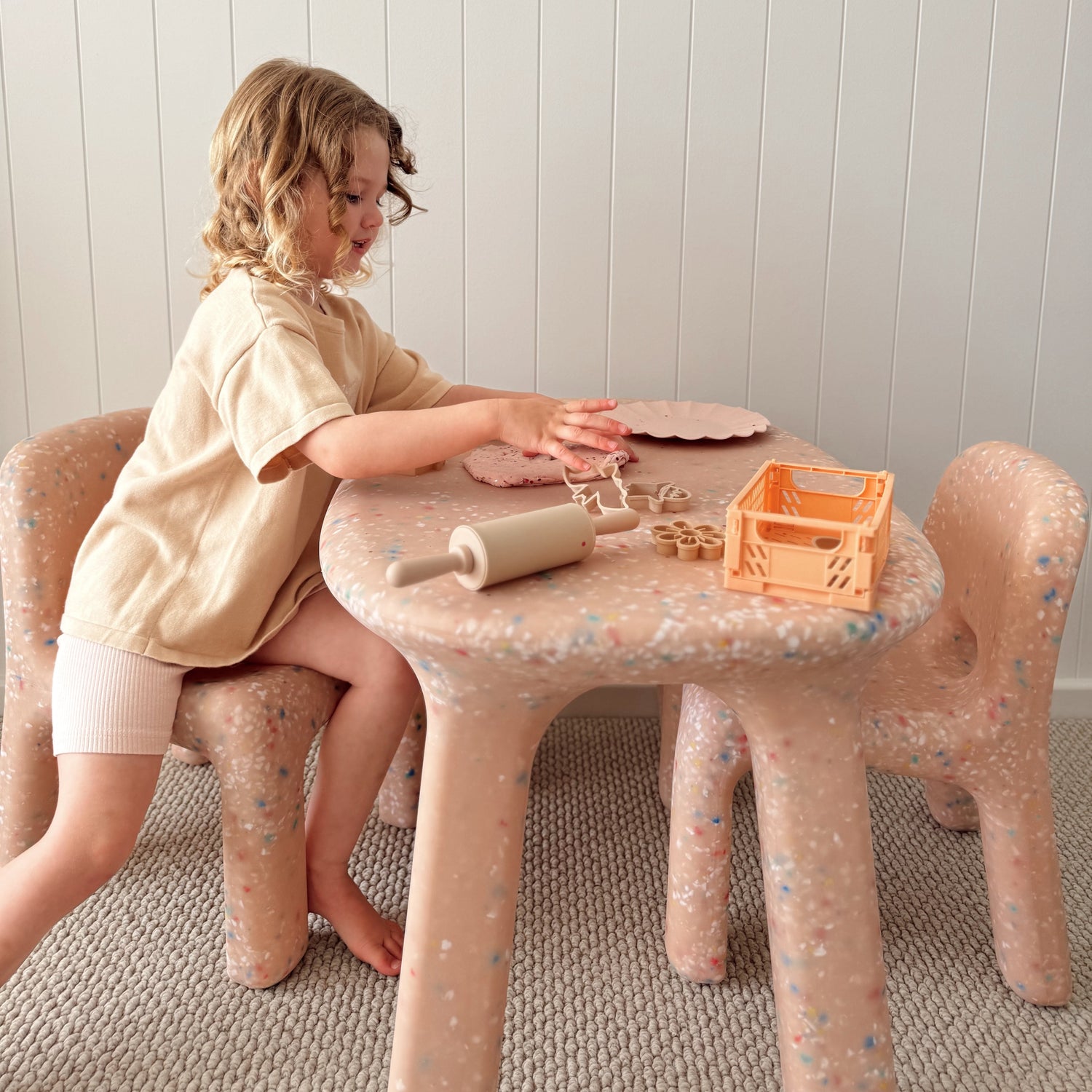 Child playing with a pink children's table and chairs in a room with a white paneled wall.